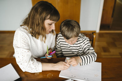 High angle view of mother teaching son with down syndrome to draw in book at table