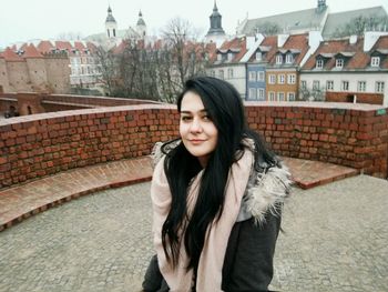 Portrait of young woman standing against brick wall