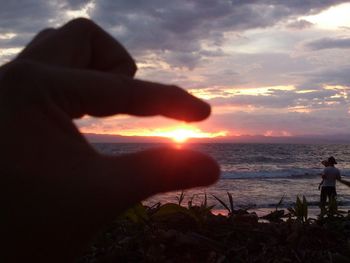 Close-up of silhouette hand on beach against sky during sunset