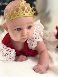 Cute baby girl in dress and crown lying on bed