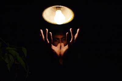 Portrait of man gesturing under illuminated light against black background