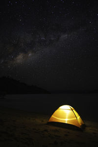 Scenic view of illuminated tent at beach against sky at night