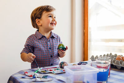 Smiling boy painting egg at home