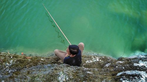 High angle view of boy fishing while sitting by lake