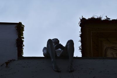 Low angle view of men sitting on abandoned building against sky