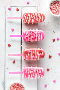 Valentine's day cakesicles on a rustic wooden board with sprinkles all around.