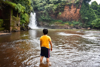 Rear view of boy standing against waterfall