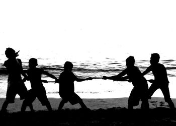 Silhouette people playing tug-of-war on beach
