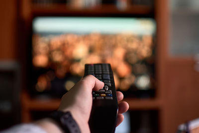 Close-up of a man changing channels with a remote control at home