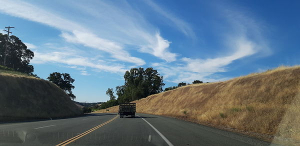 Road by trees against sky