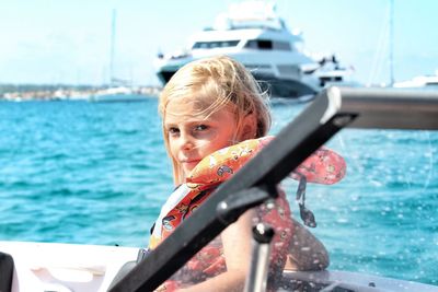 Portrait of cute girl wearing life jacket sitting on boat in sea