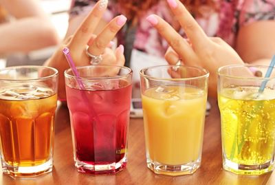 Midsection of woman gesturing peace sign by drink glasses on table
