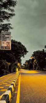 Road sign by trees against sky