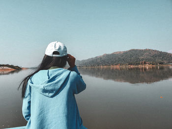 Rear view of woman looking at lake against clear sky