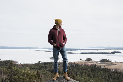 Man standing on a rock whilst hiking a hill above the ocean in sweden