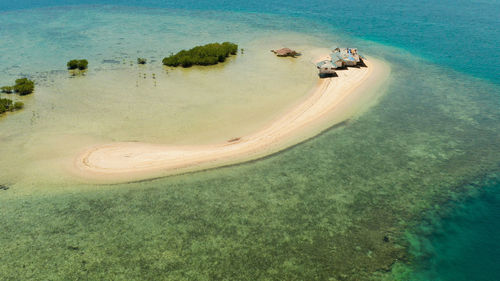 Sandy island with sand bar surrounded by coral reef and blue sea in honda bay, aerial view. 