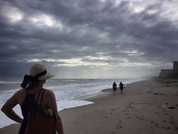 Rear view of people standing on beach against sky