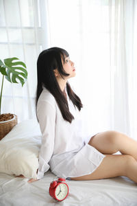 Young woman sitting on bed with clock