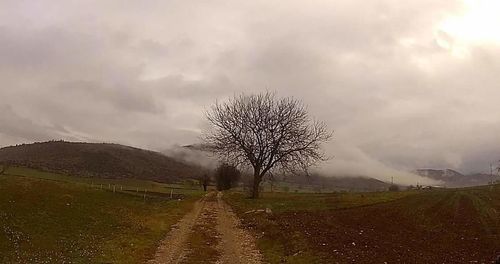 Road passing through field against cloudy sky