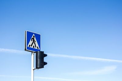 Low angle view of road sign and stoplight against blue sky