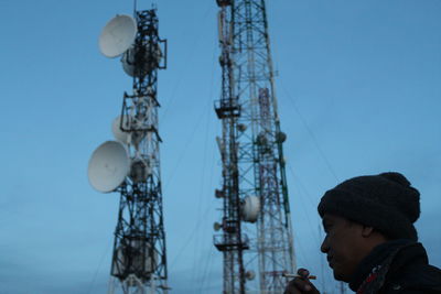 Man smoking cigarette against communications tower and blue sky