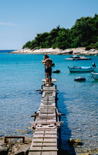 Rear view of man standing on pier by sea against sky