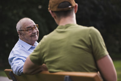 Portrait of smiling senior man relaxing together with his grandson on a park bench