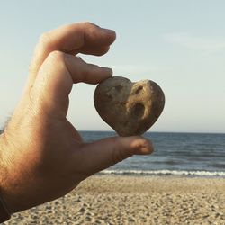 Close-up of hand holding heart shape on beach