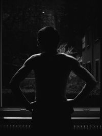 Rear view of shirtless man standing against trees at night