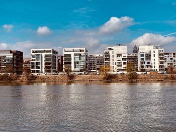 Buildings by river against blue sky