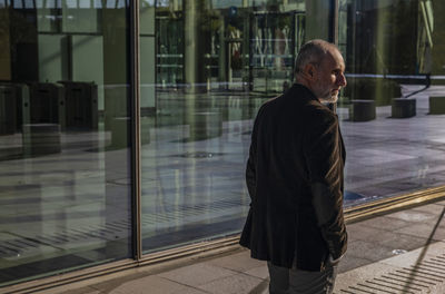 Portrait of adult man in suit against glass wall, city business district