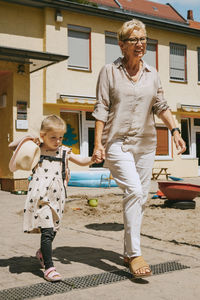 Grandmother with granddaughter walking on footpath in front of kindergarten