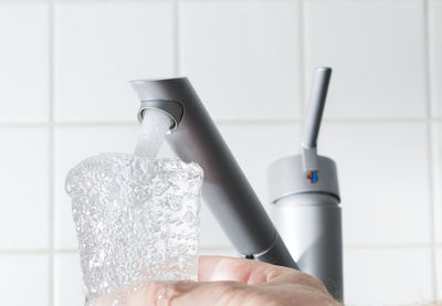 Cropped hand of man holding glass under faucet