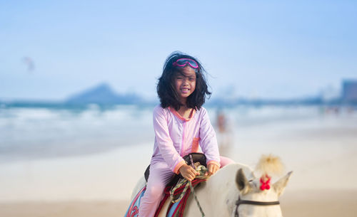 Girl riding on howoman wearing mask on beach against sky