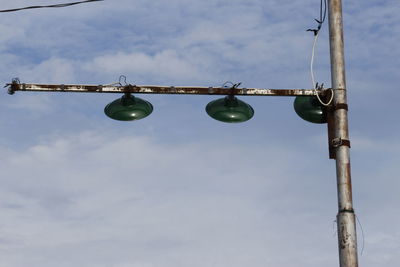 Low angle view of light bulbs hanging on pole against sky