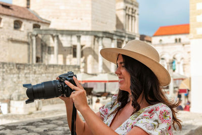 Woman holding a camera taking a photo in front of an ancient building in split, croatia