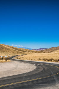 Road by desert against clear blue sky