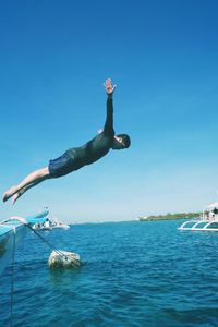 Man jumping in sea against clear blue sky