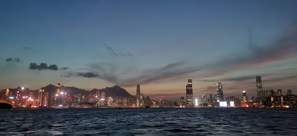 Illuminated buildings by sea against sky at night