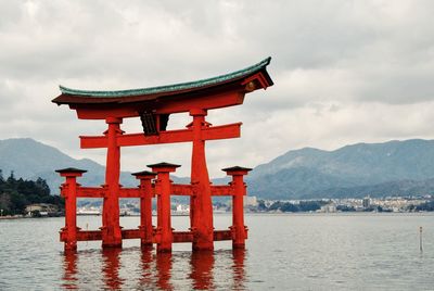 Torii gate in sea at itsukushima shrine against sky