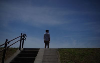 Rear view of man standing on steps against sky