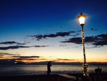 Silhouette illuminated light on beach against sky at sunset