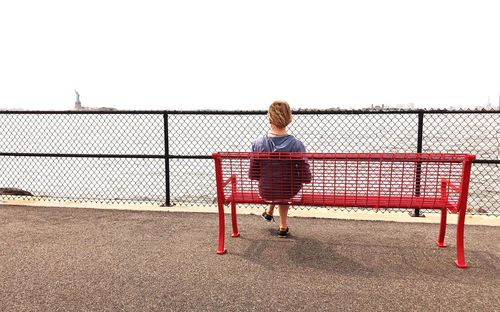 Rear view of woman standing on railing against clear sky