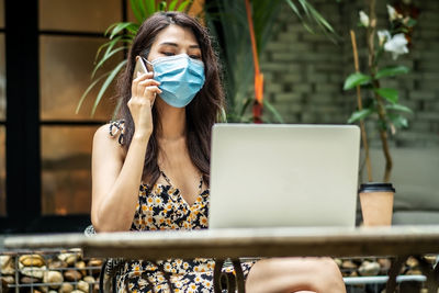 Young woman wearing mask while using phone at cafe