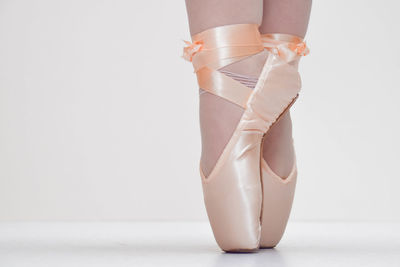 Low section of woman with ballet shoes against white background