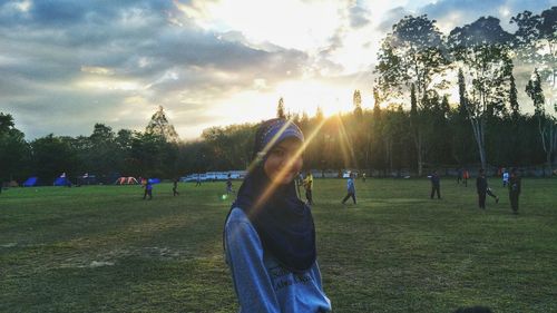 People on field by trees against sky during sunset