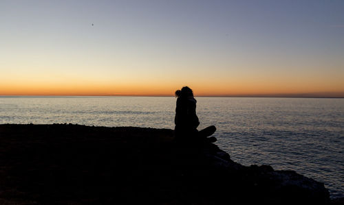 Silhouette man looking at sea against sky during sunset