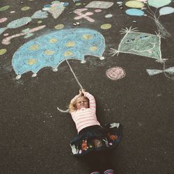 High angle view of girl lying by drawing on road