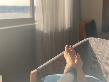 Low section of woman relaxing on window at home