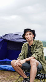 Young man sitting on car against sky